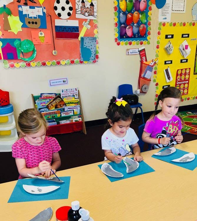 Three children doing crafts at a table in a classroom