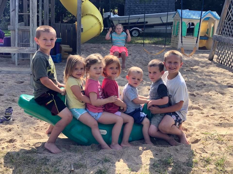Children sitting on a green seesaw toy in a sandy area