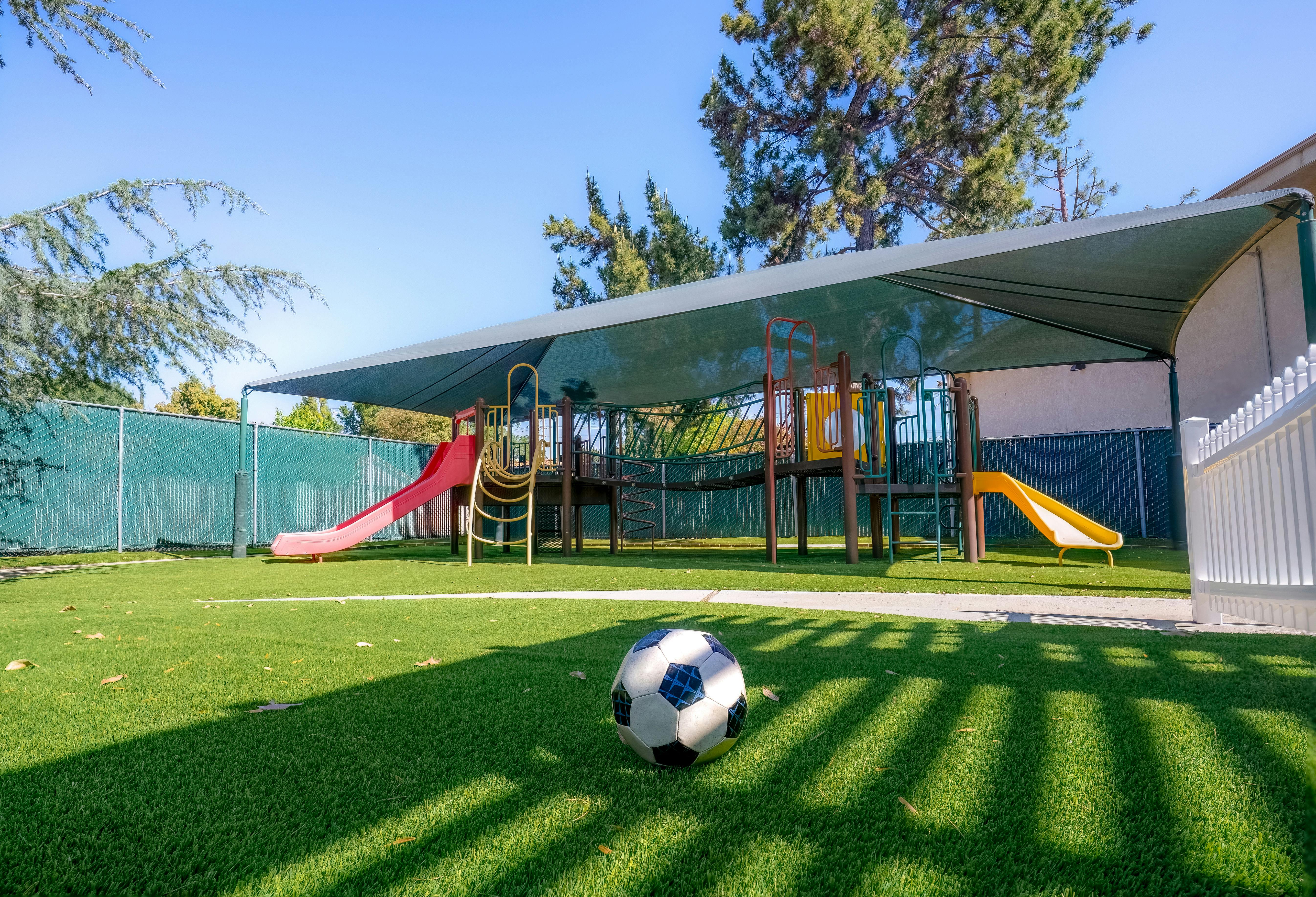 Soccer ball on artificial turf in front of a playground with slides