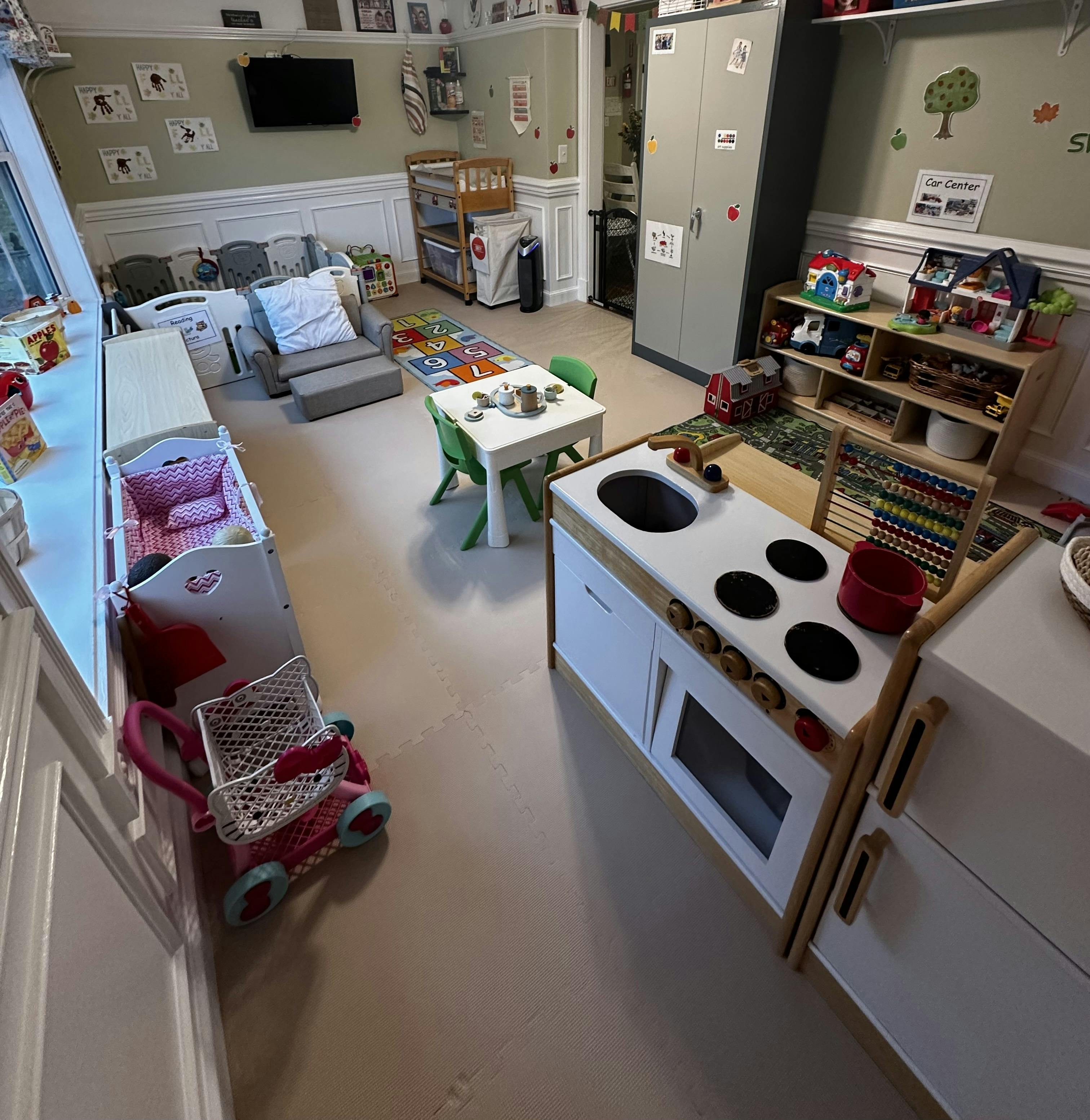 Playroom with toy kitchen, small table and chairs, and crib