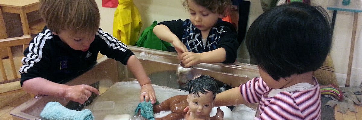 Three children playing with a doll in a water table