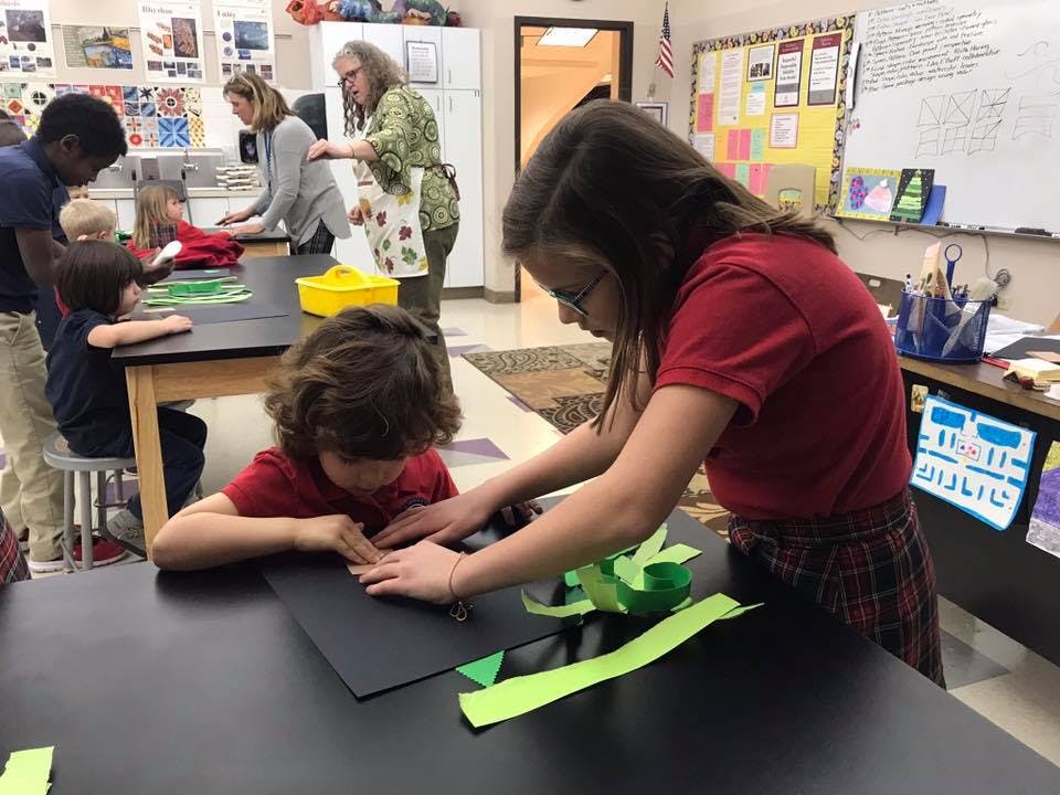 Two children working on a craft project with green paper strips