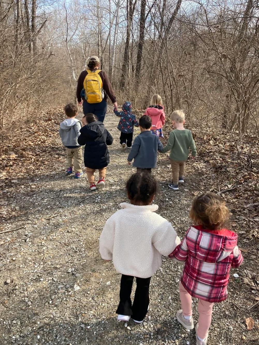 A person leading a group of children walking along a wooded trail