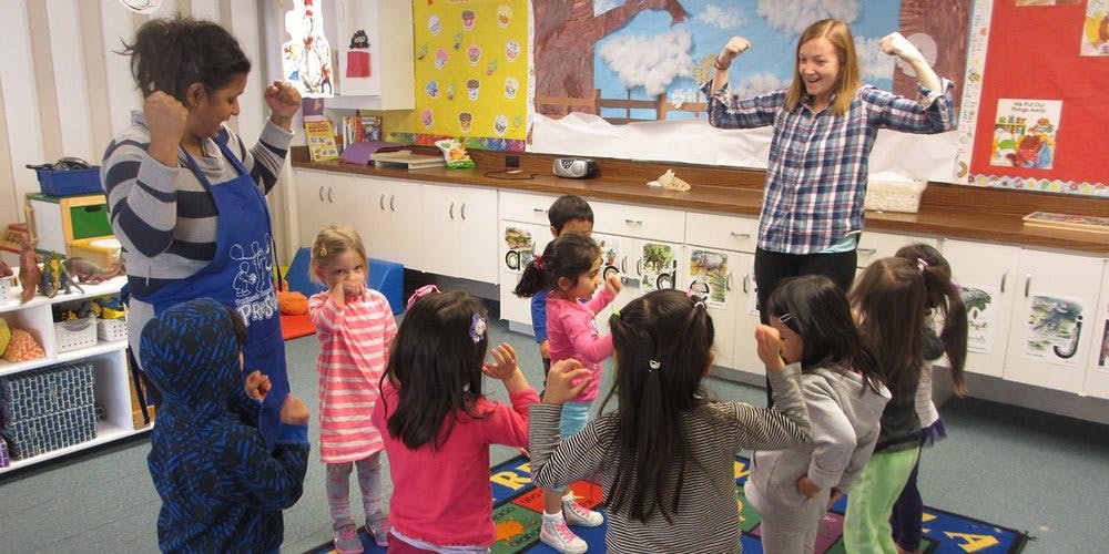 Two people leading a group of children in an activity in a classroom