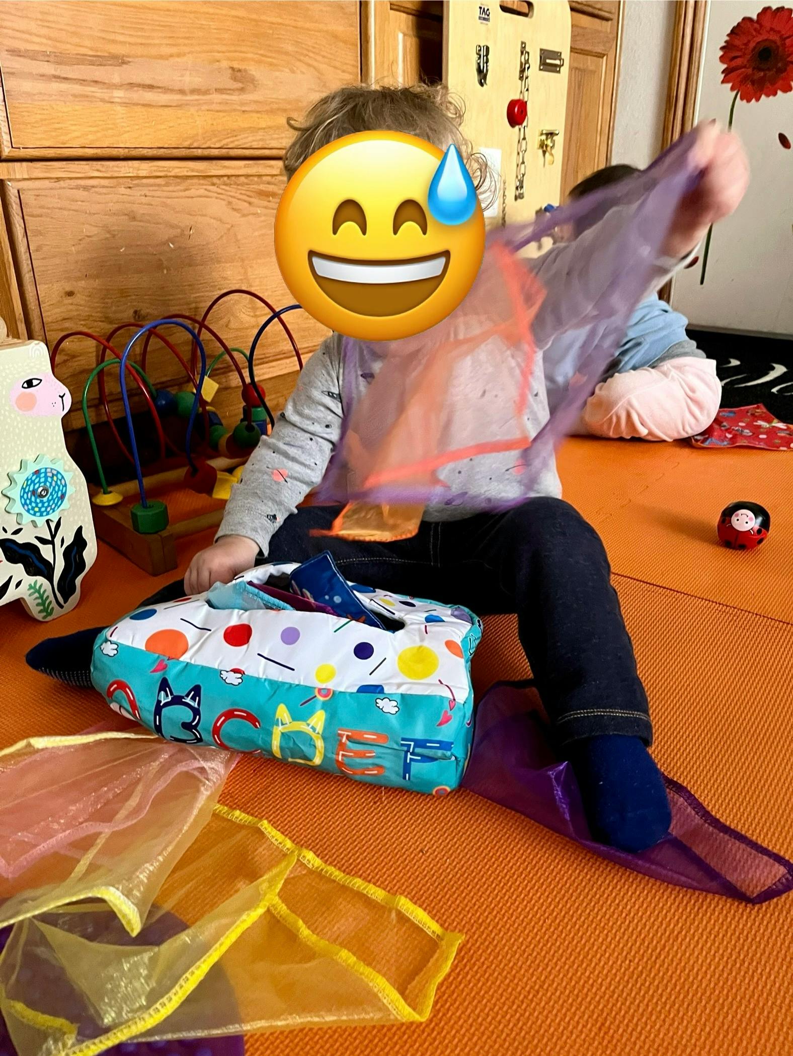 Child playing with colorful scarves and a tissue box toy