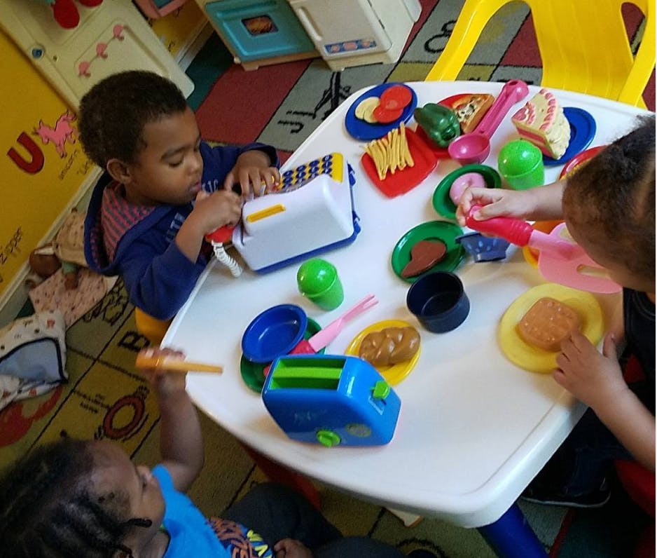 Children playing with toy food and kitchen items at a small table