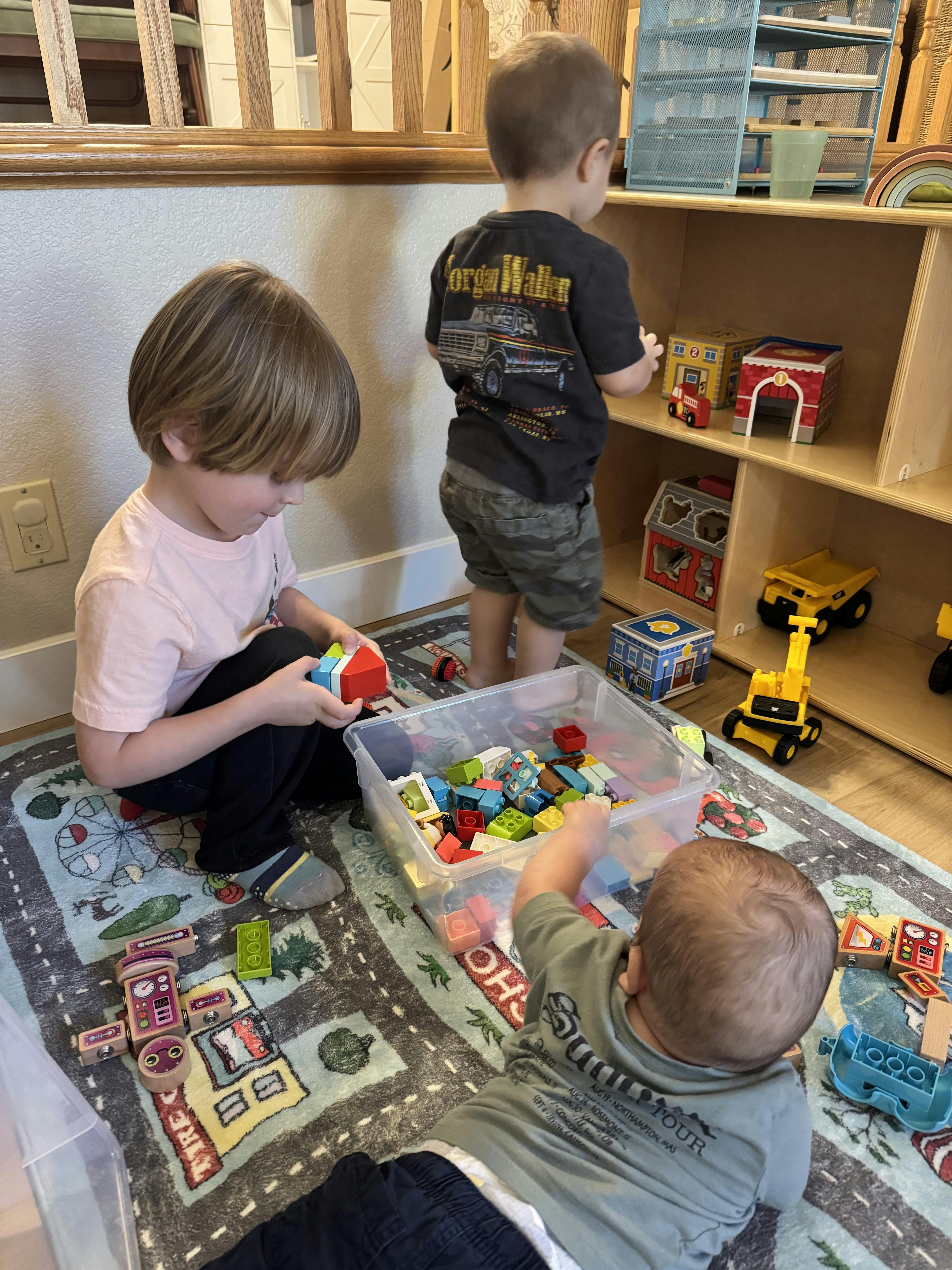 Three children playing with blocks and toys on a road-themed rug