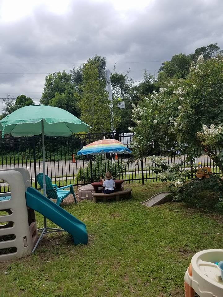 Child sitting at a small picnic table under an umbrella in a grassy yard
