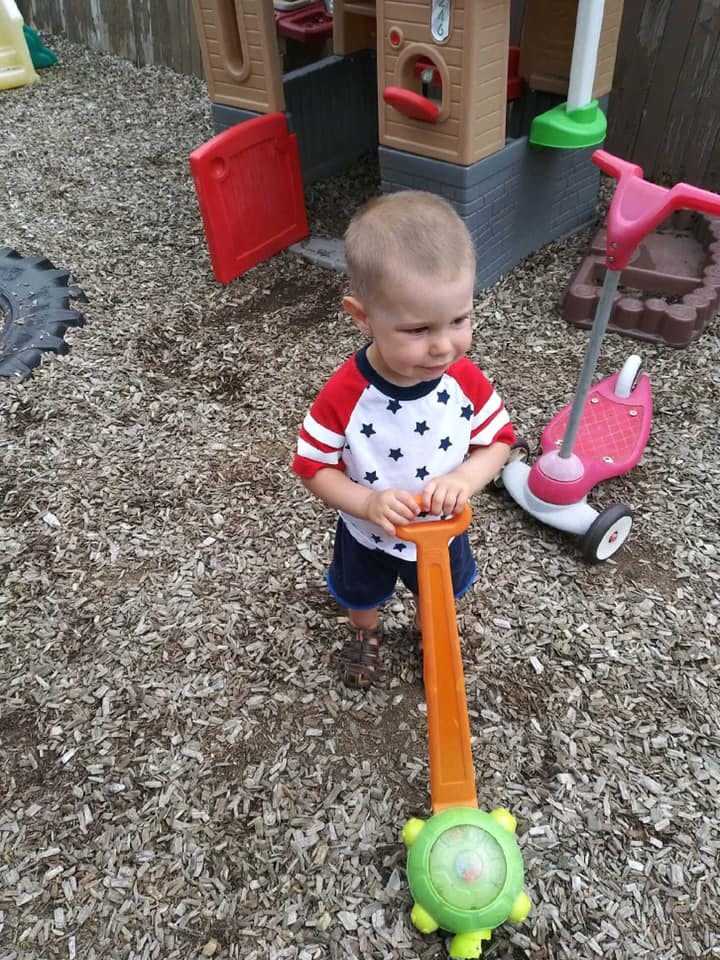 Child holding a toy push mower on wood chips