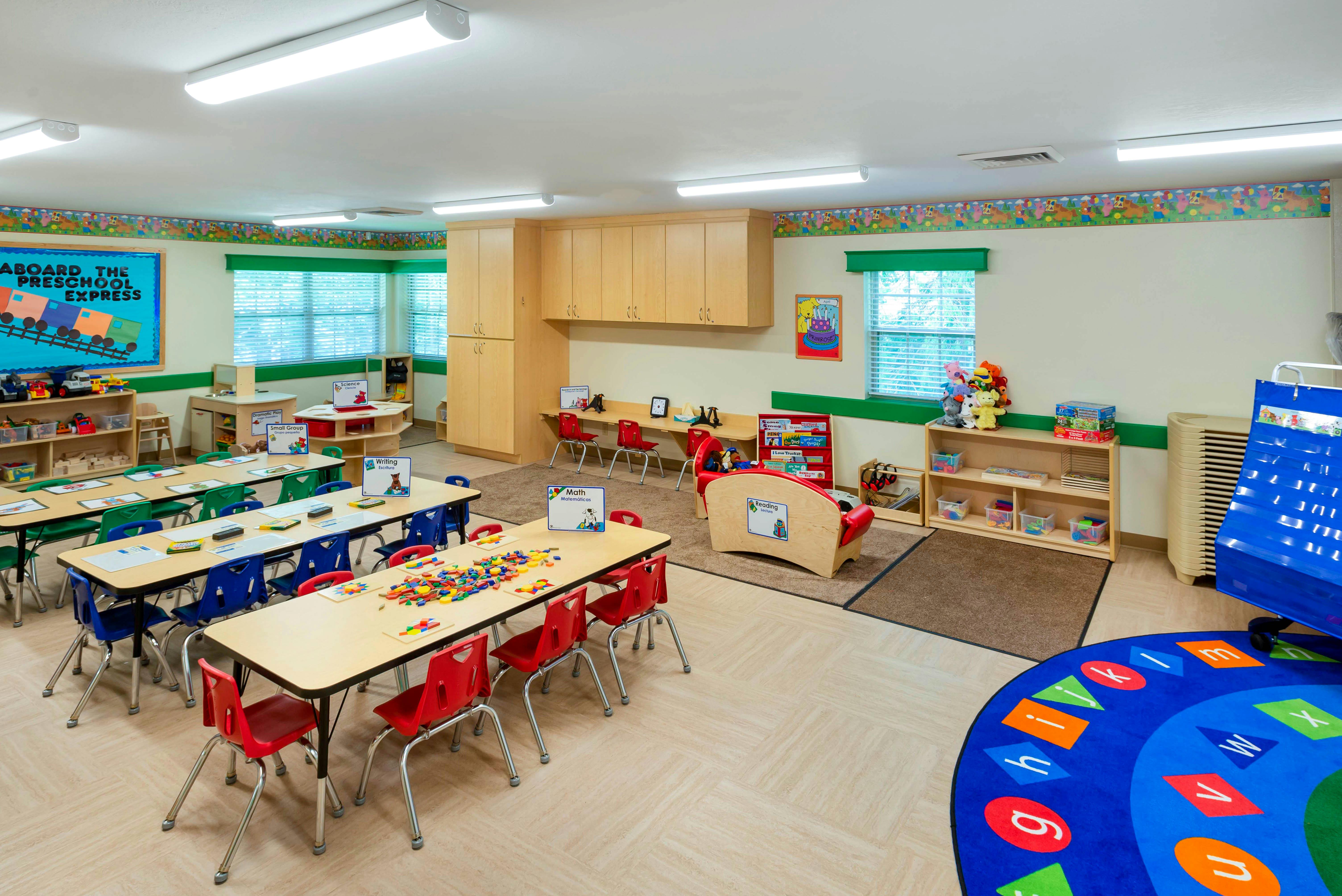 A colorful preschool classroom with tables, chairs, a reading corner, and play areas