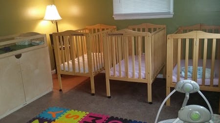 Multiple wooden cribs in a room with a colorful playmat