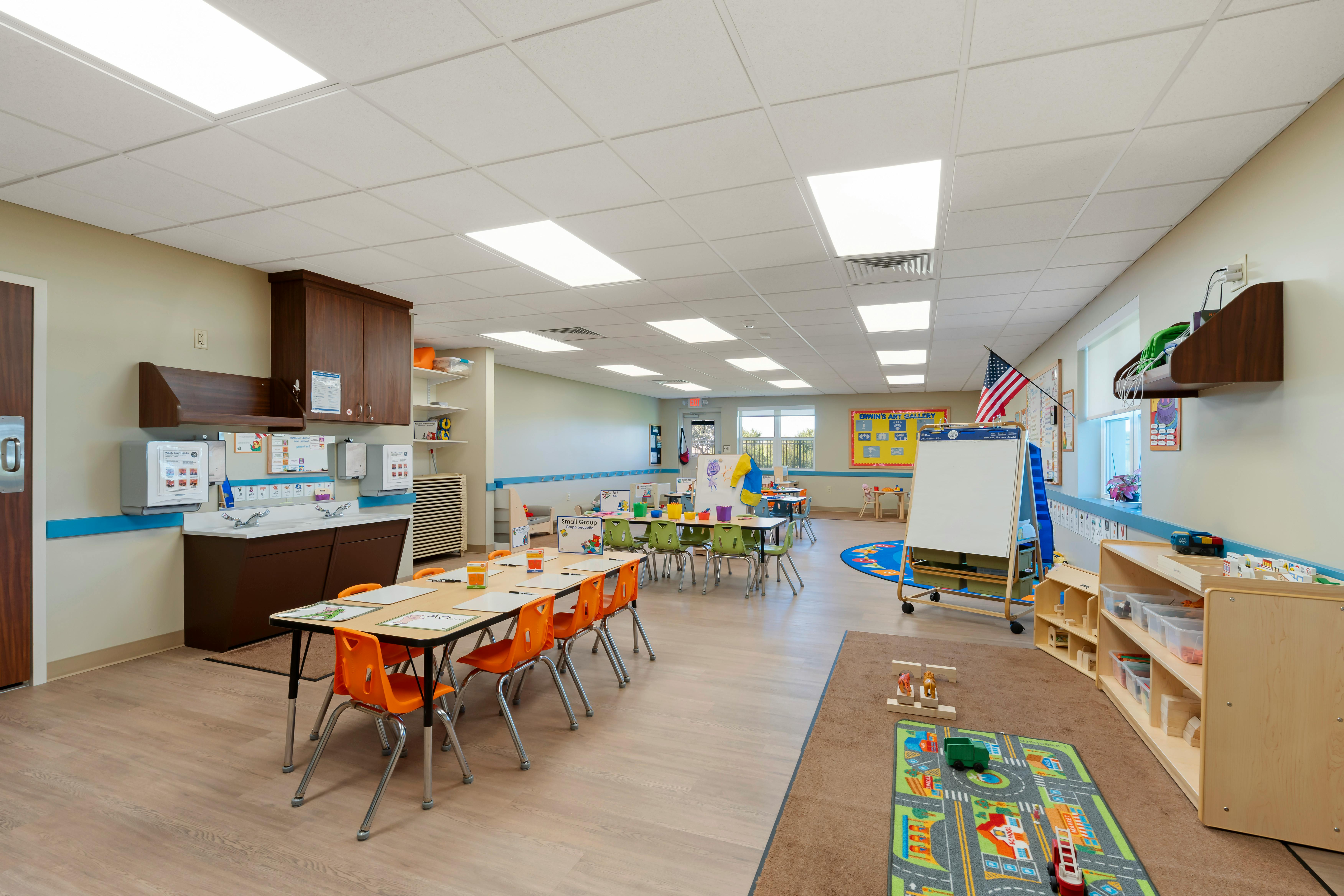 Classroom with tables and chairs for children, a sink area, and toys