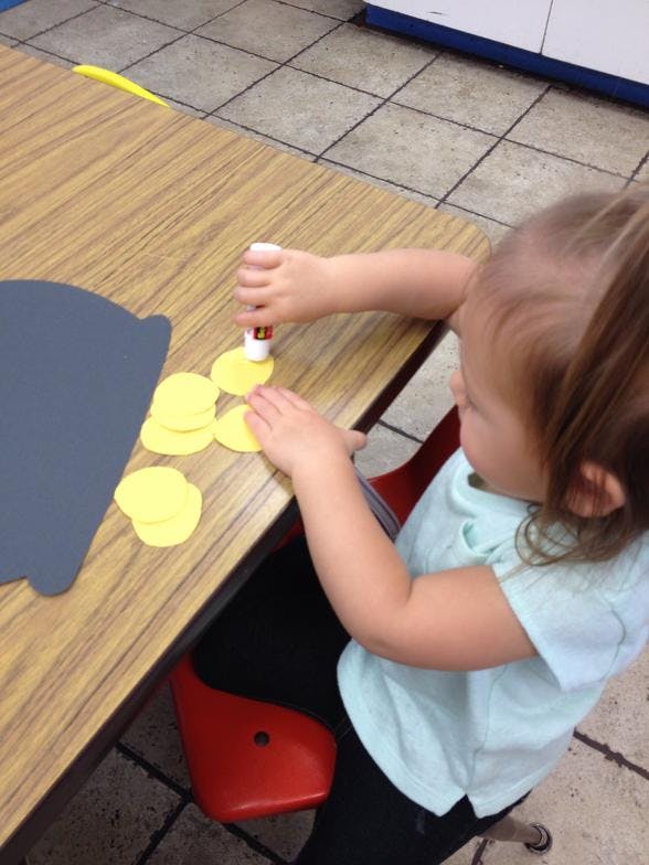 Child gluing yellow paper circles onto a gray shape at a table