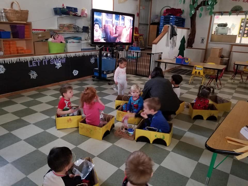 Children sitting in yellow boxes watching a television