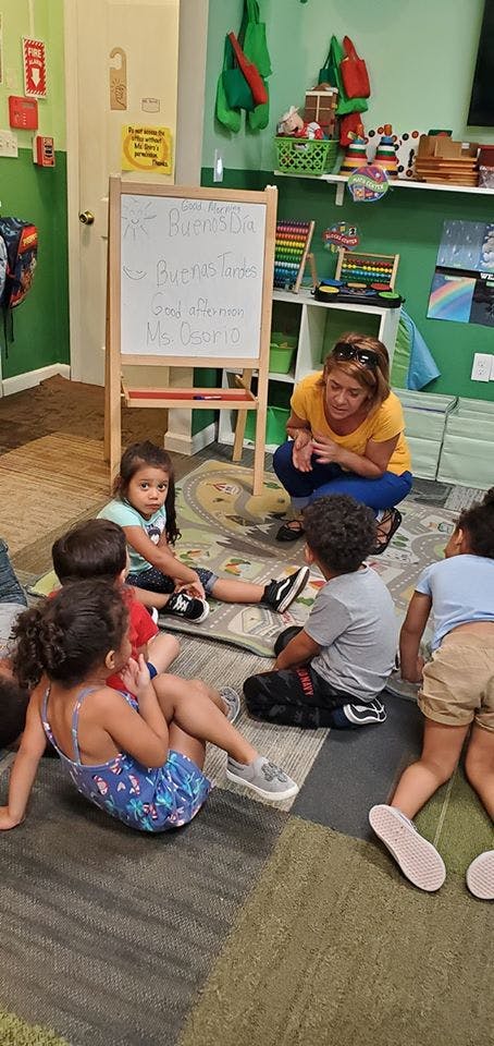 Adult person crouching with children sitting on a rug in a classroom