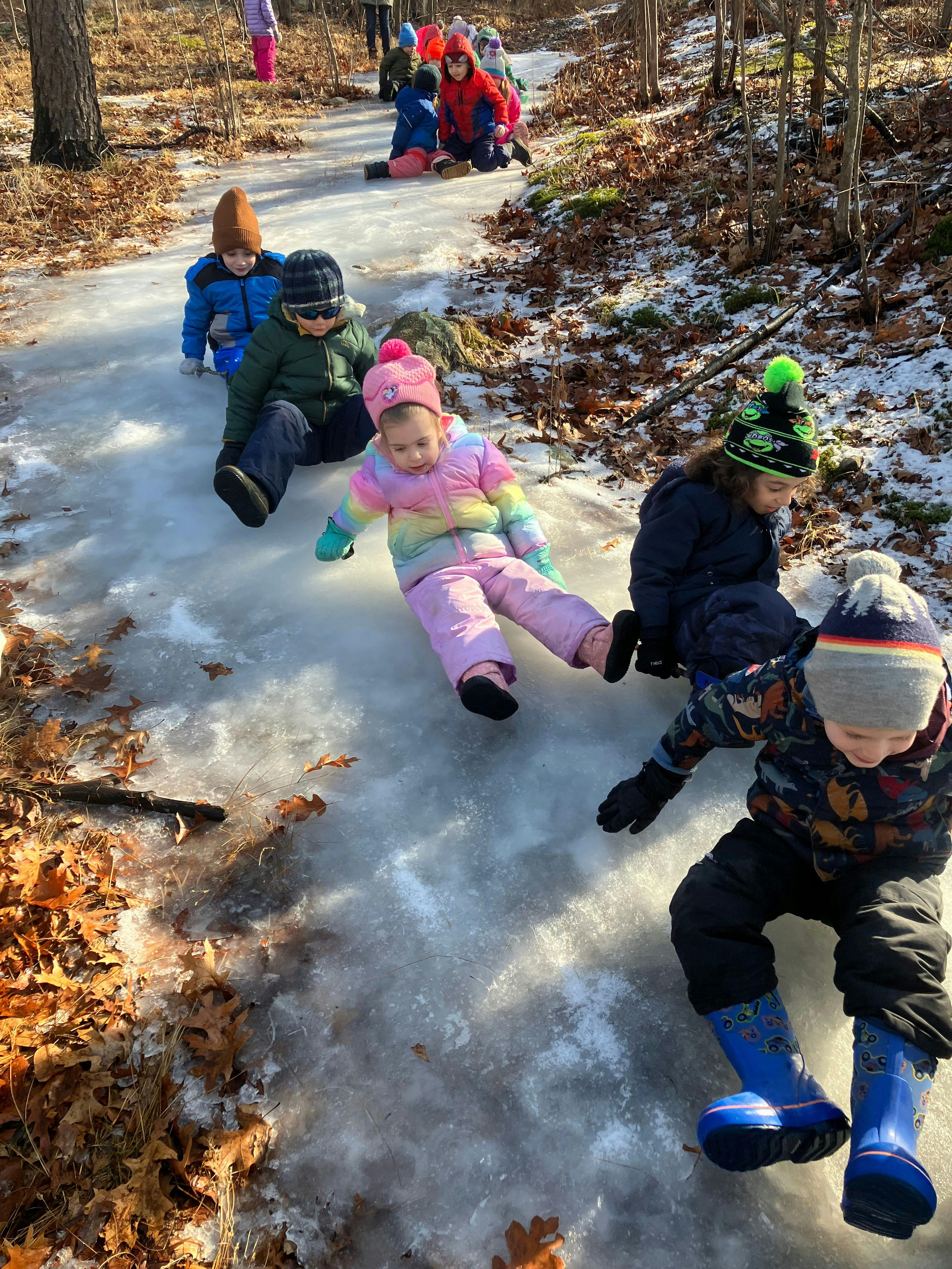 Children sliding down an icy path in the woods