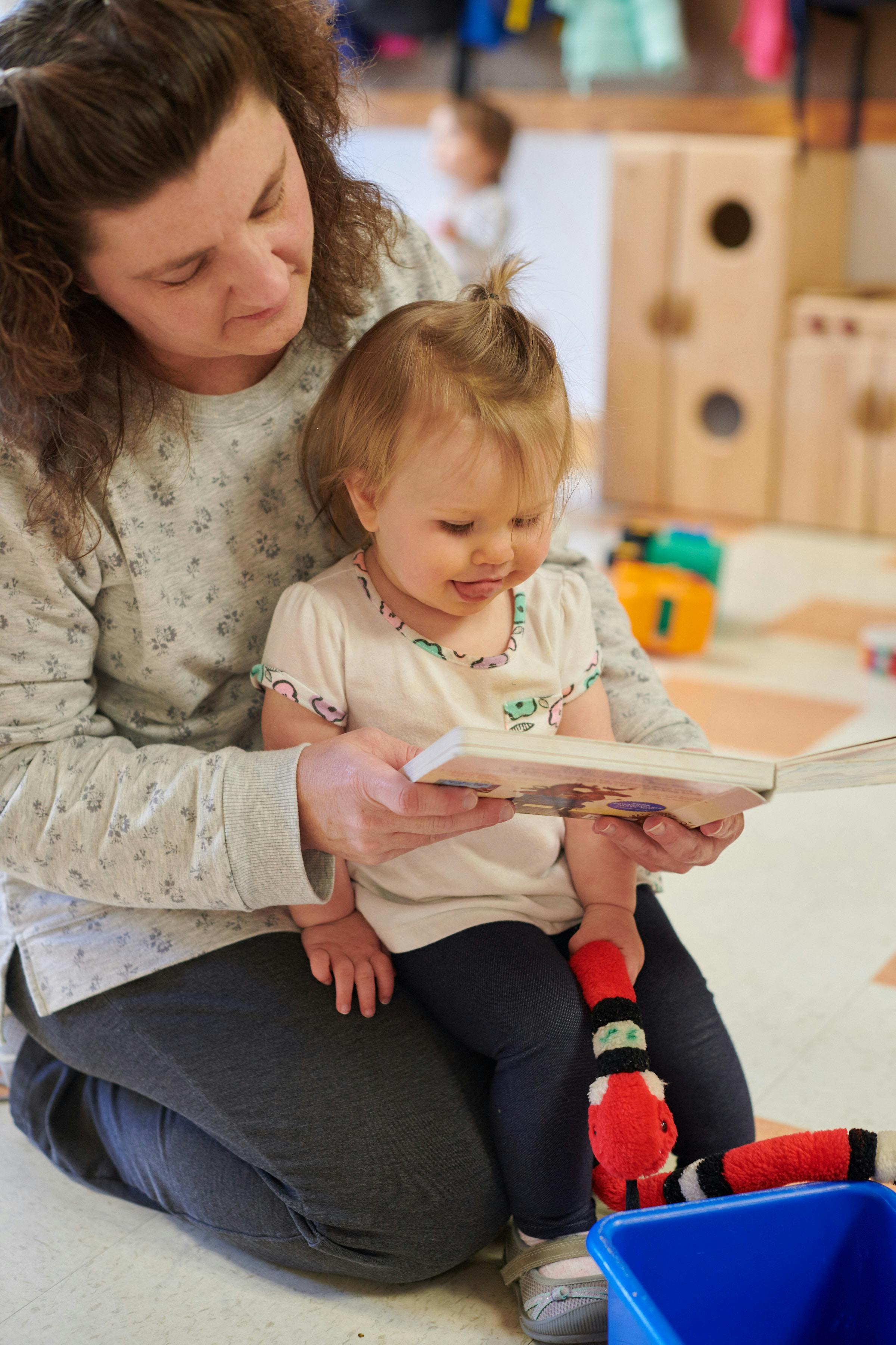 Person kneeling and holding a book for a child sitting on their lap