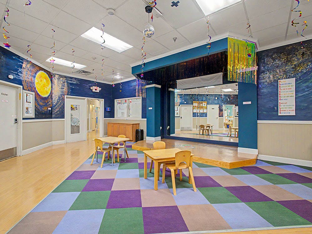 Classroom with checkered carpet, small tables, and a stage with mirrored wall