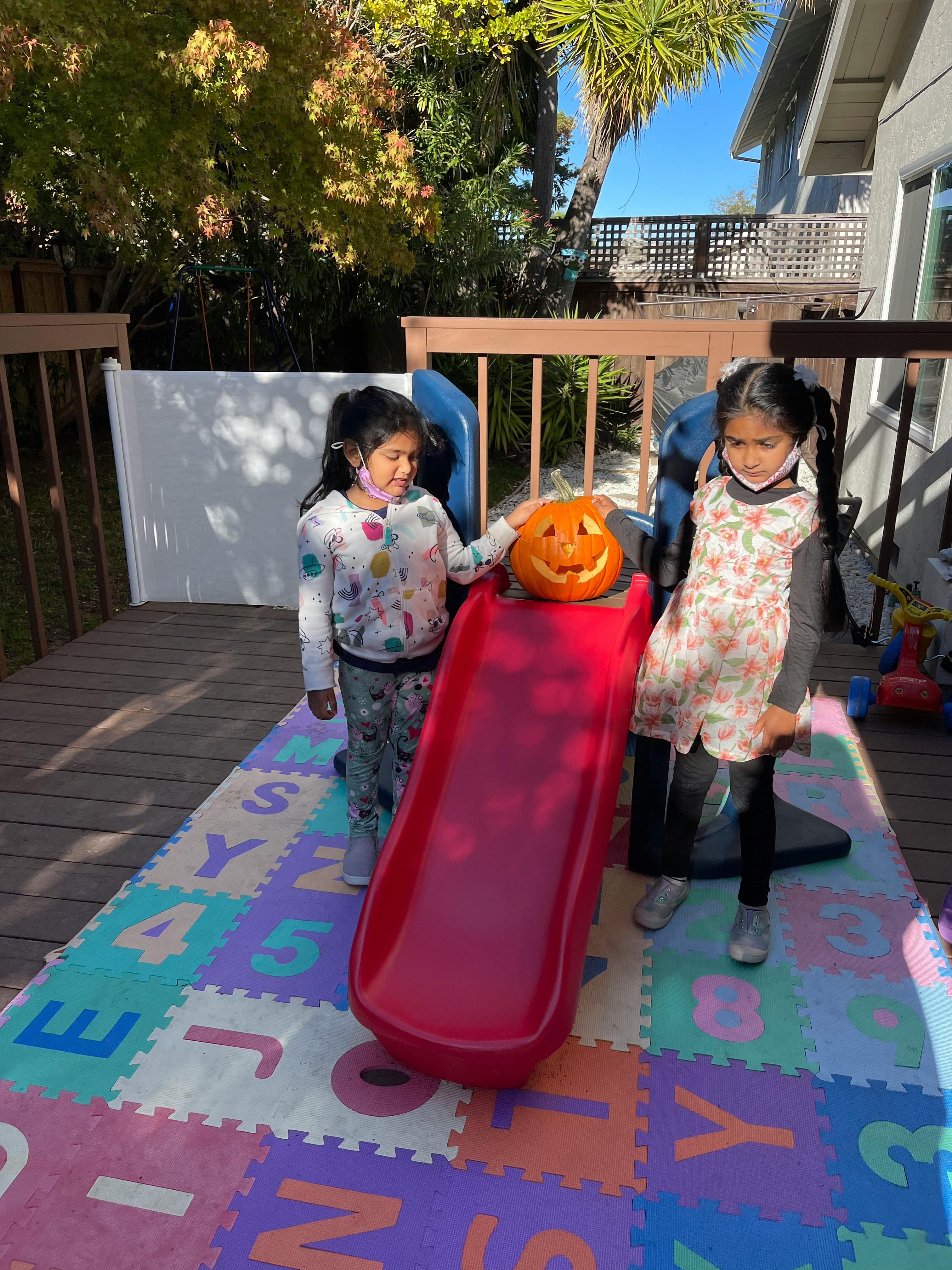 Two children with a jack-o'-lantern on a red slide