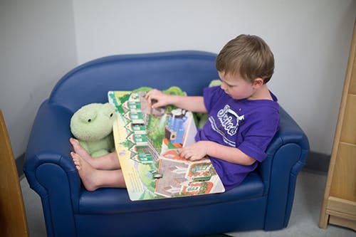 Child sitting on a blue couch reading a book