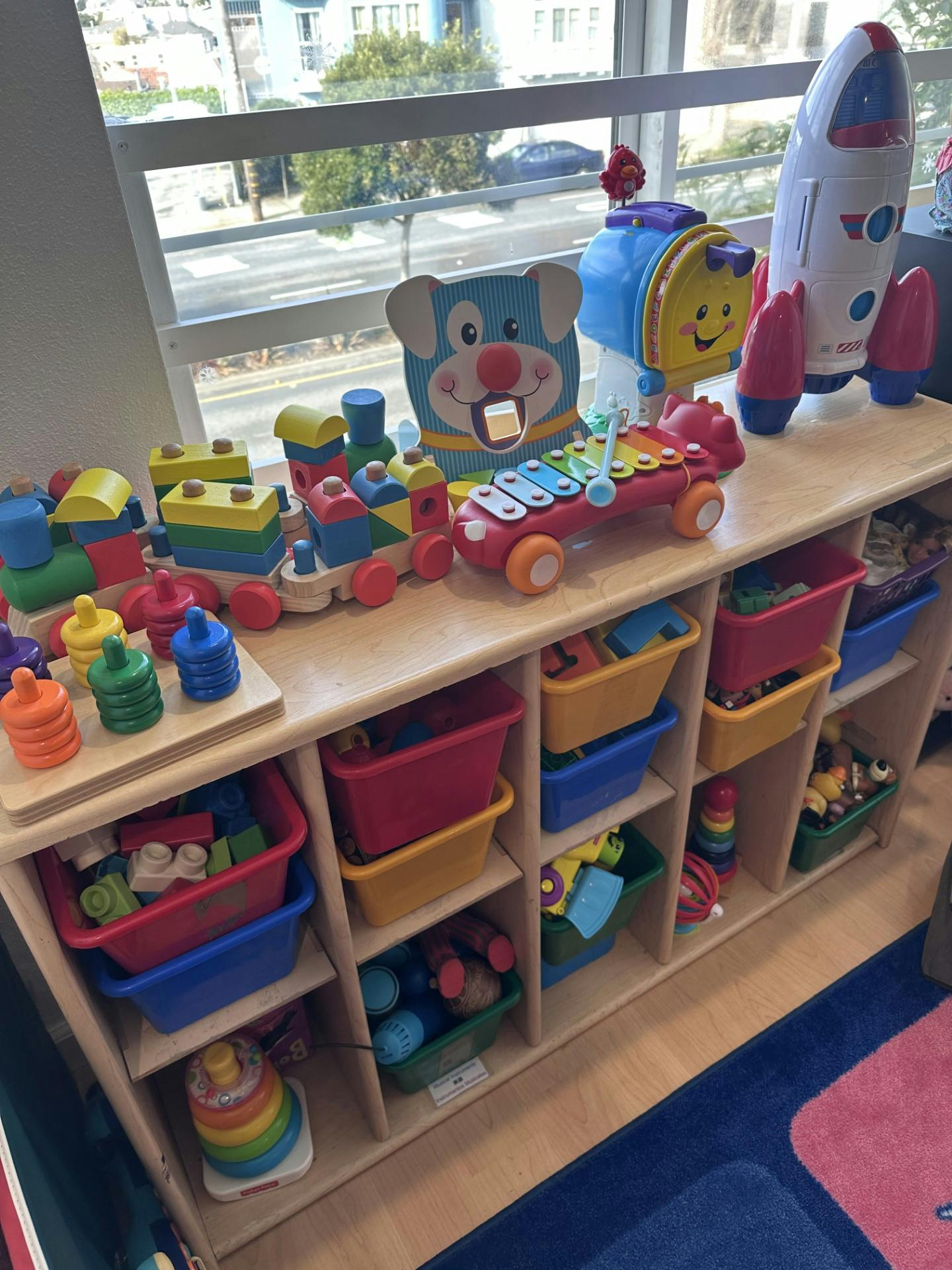 Shelf with various toys including a wooden train, xylophone, and rocket