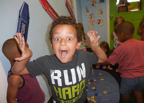 Child with mouth open and hands raised, wearing a shirt that says "RUN HARD"