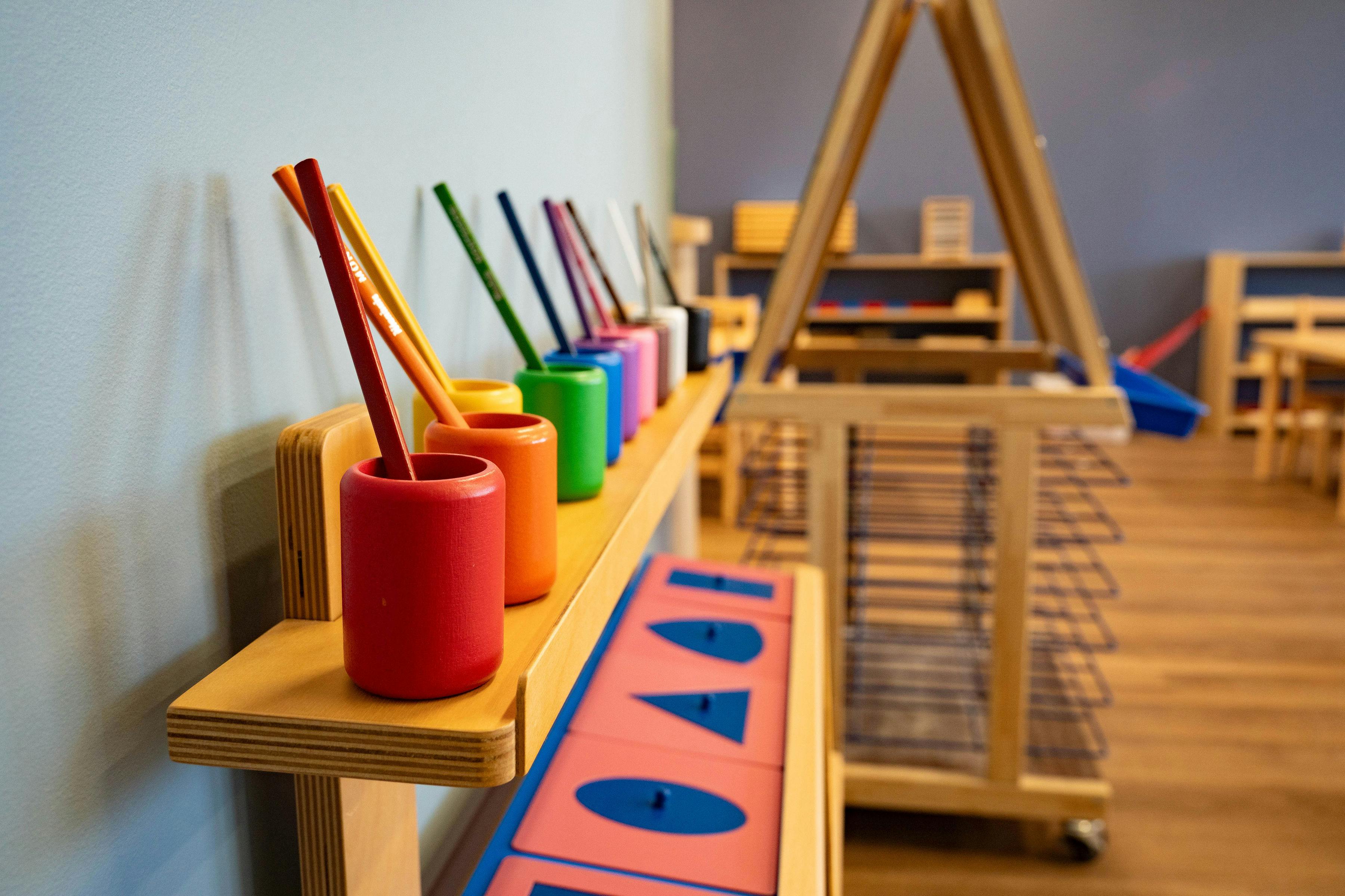 Colorful pencils in cups on a wooden shelf in a classroom