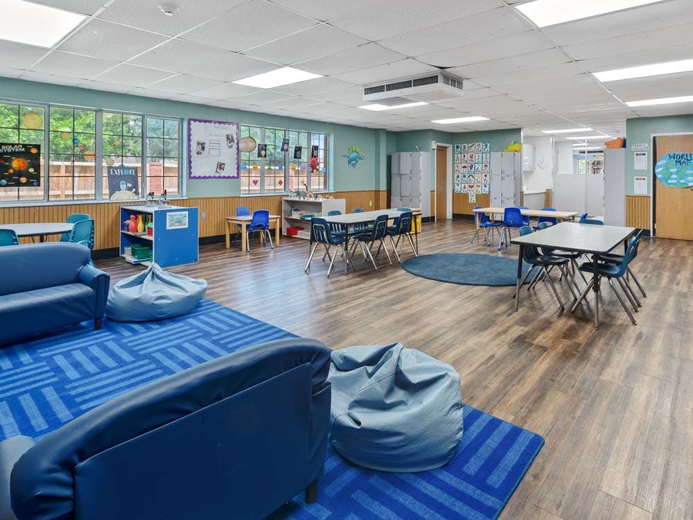 Classroom with blue furniture, small tables, and a blue rug