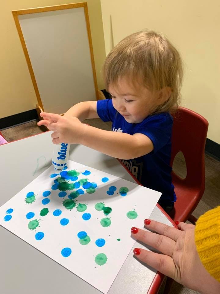 Child making blue and green dots on paper with a paint dauber