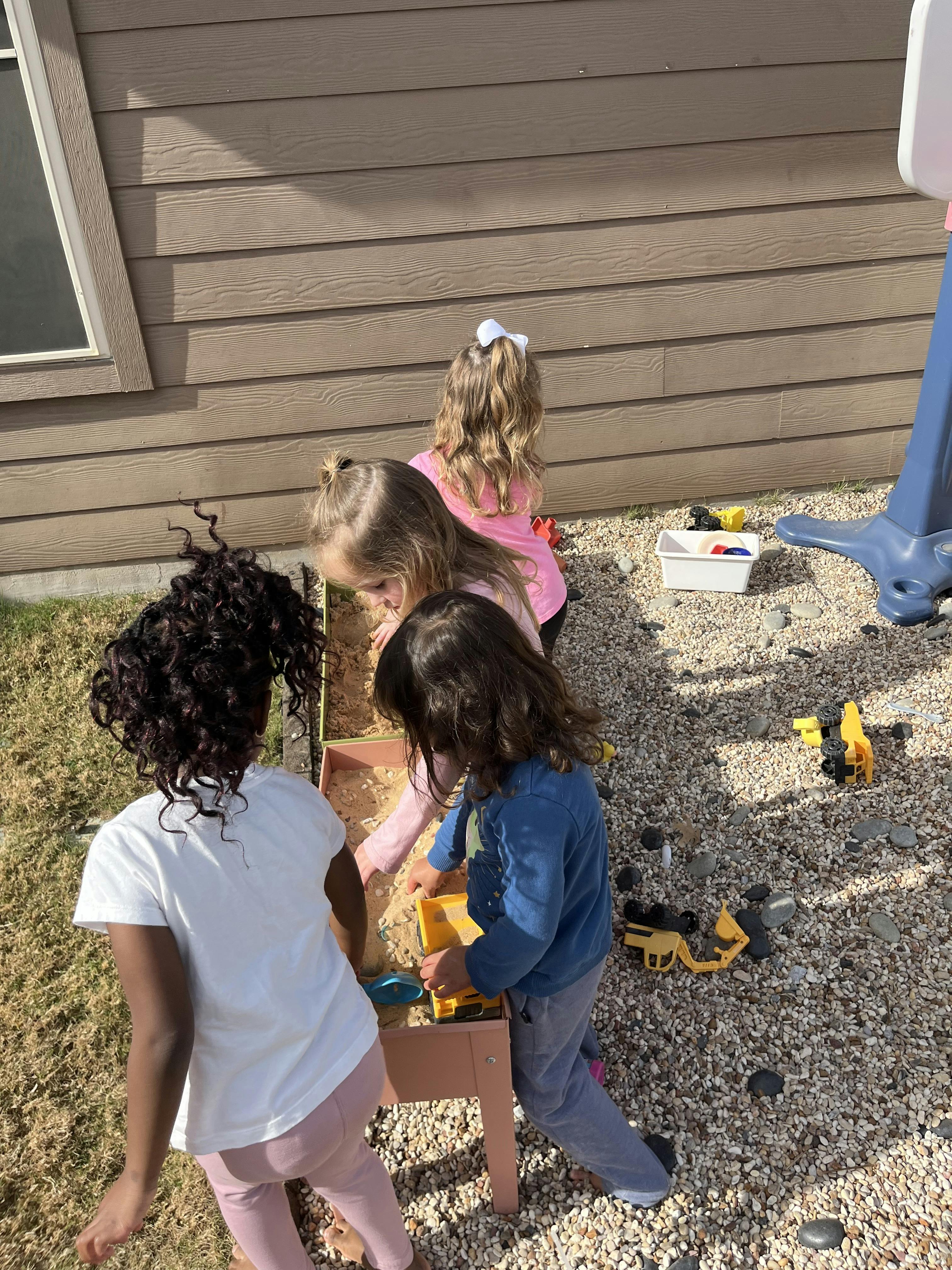 Three children playing with toys in a gravel area