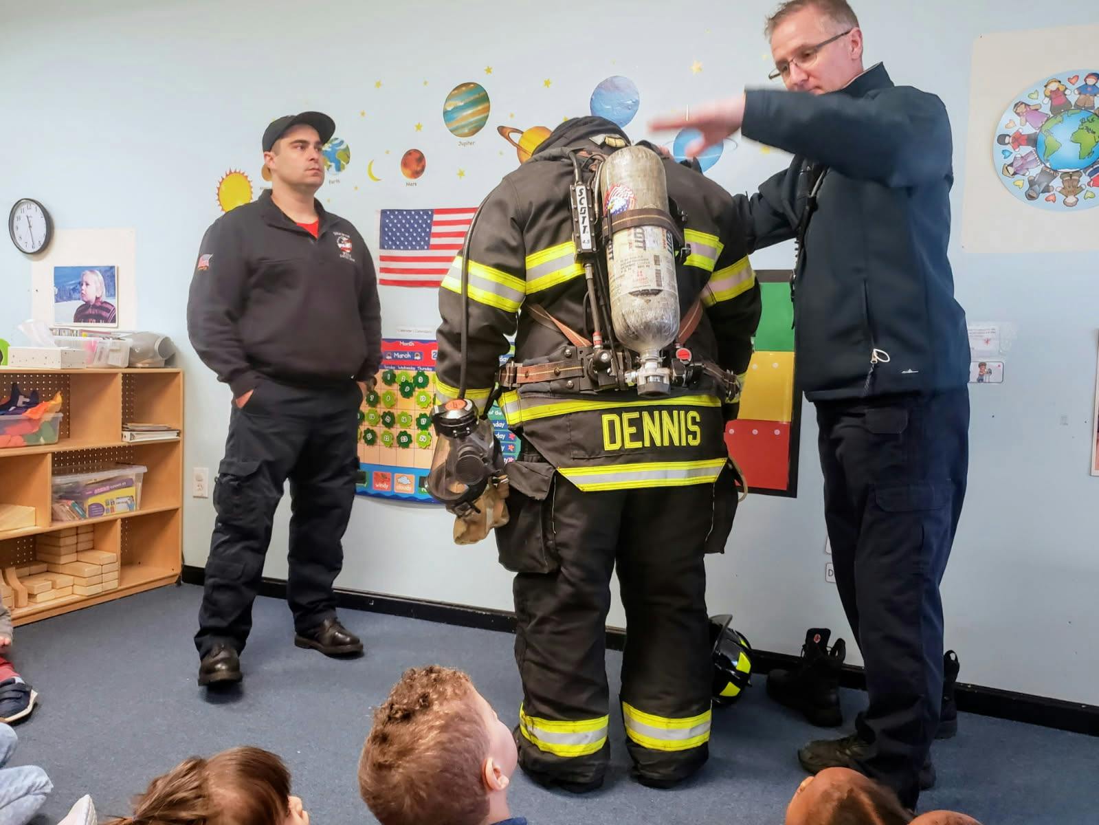 Firefighter in uniform with air tank, another person pointing, and children observing