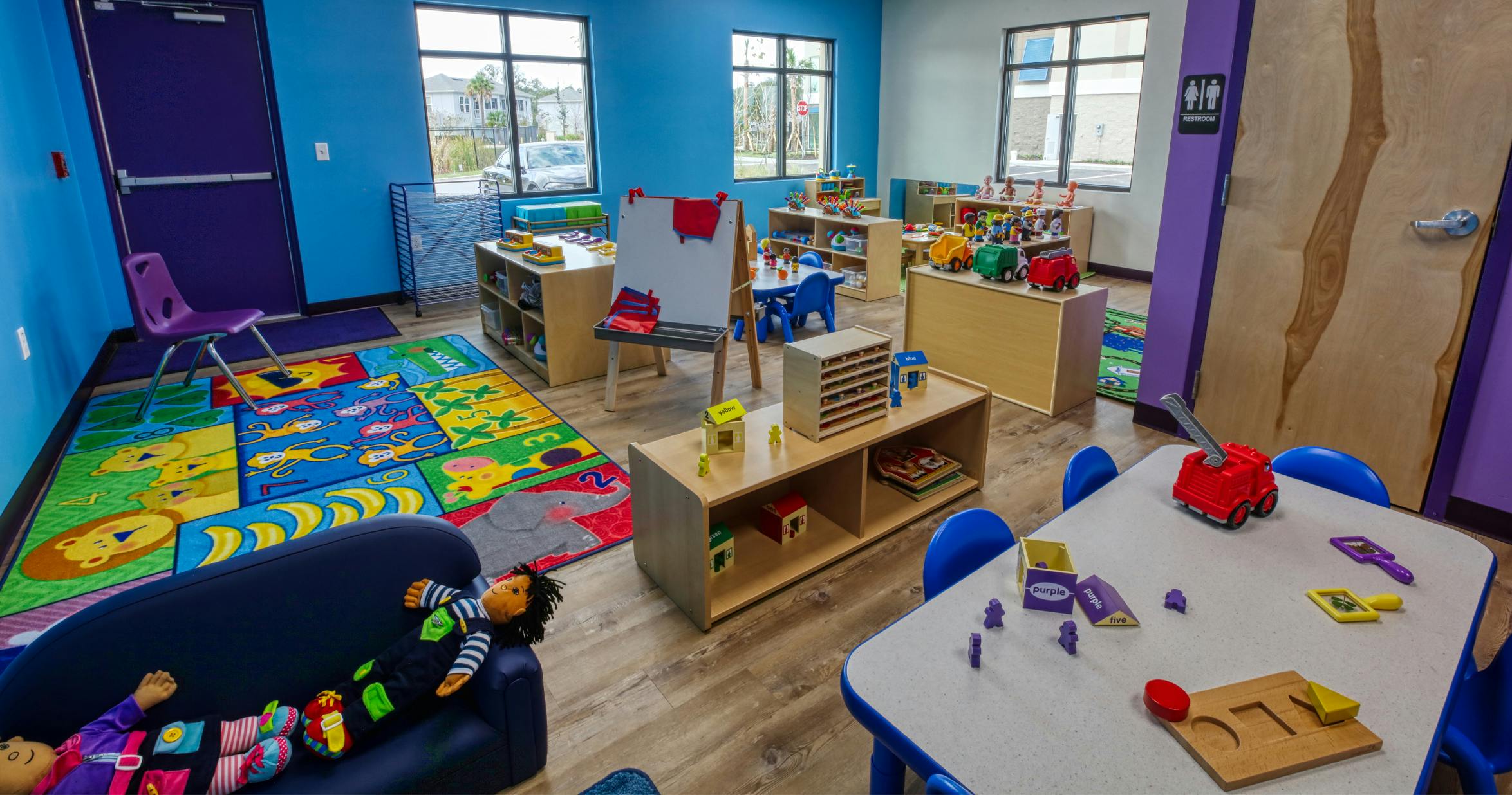 Classroom with small tables and chairs, toys, and colorful playmats