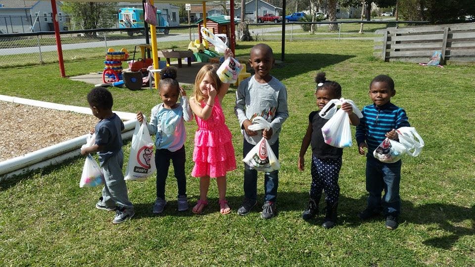 Six children standing on grass holding bags