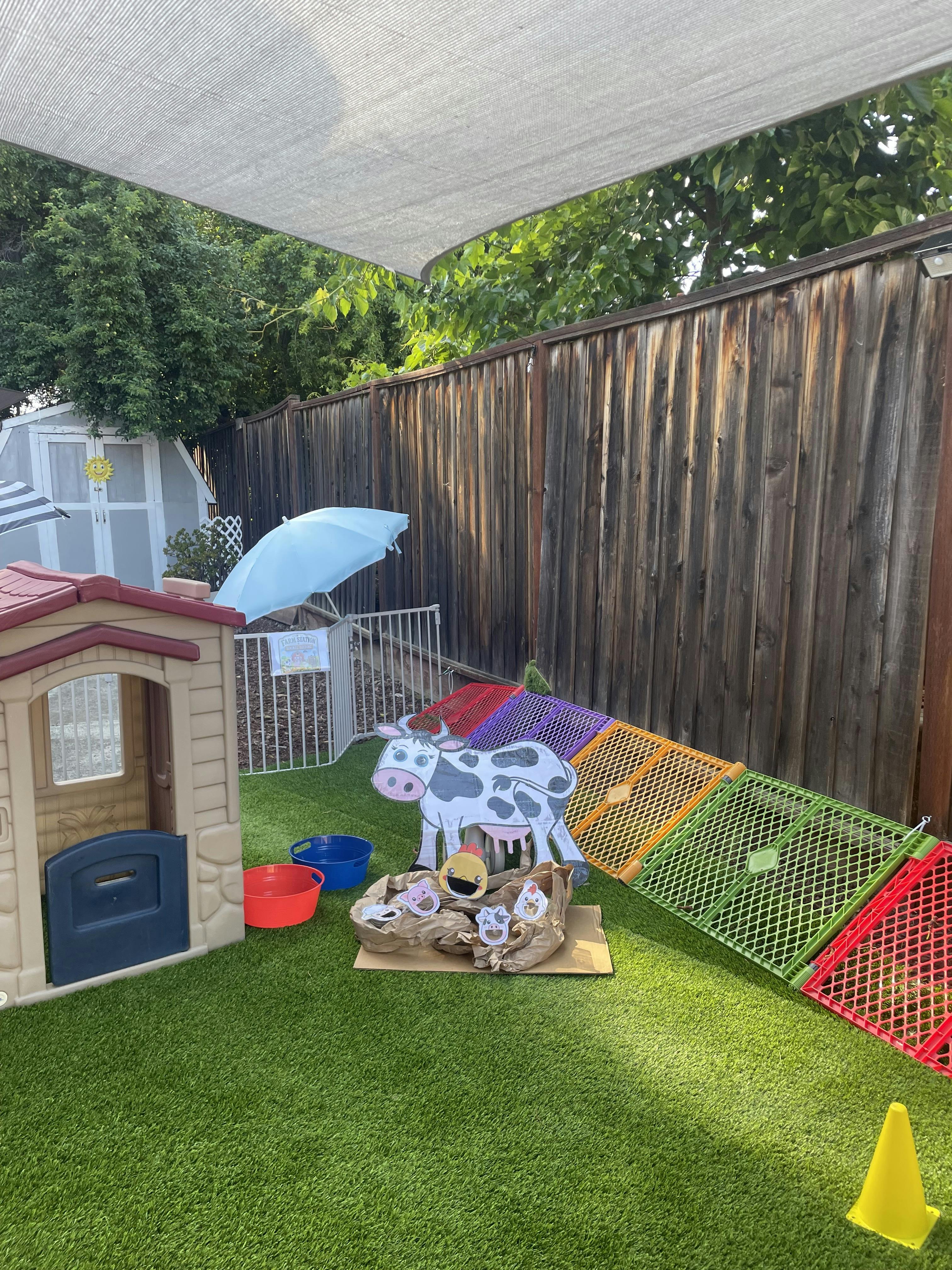 Outdoor play area with a toy house, a cow cutout, and colorful barriers