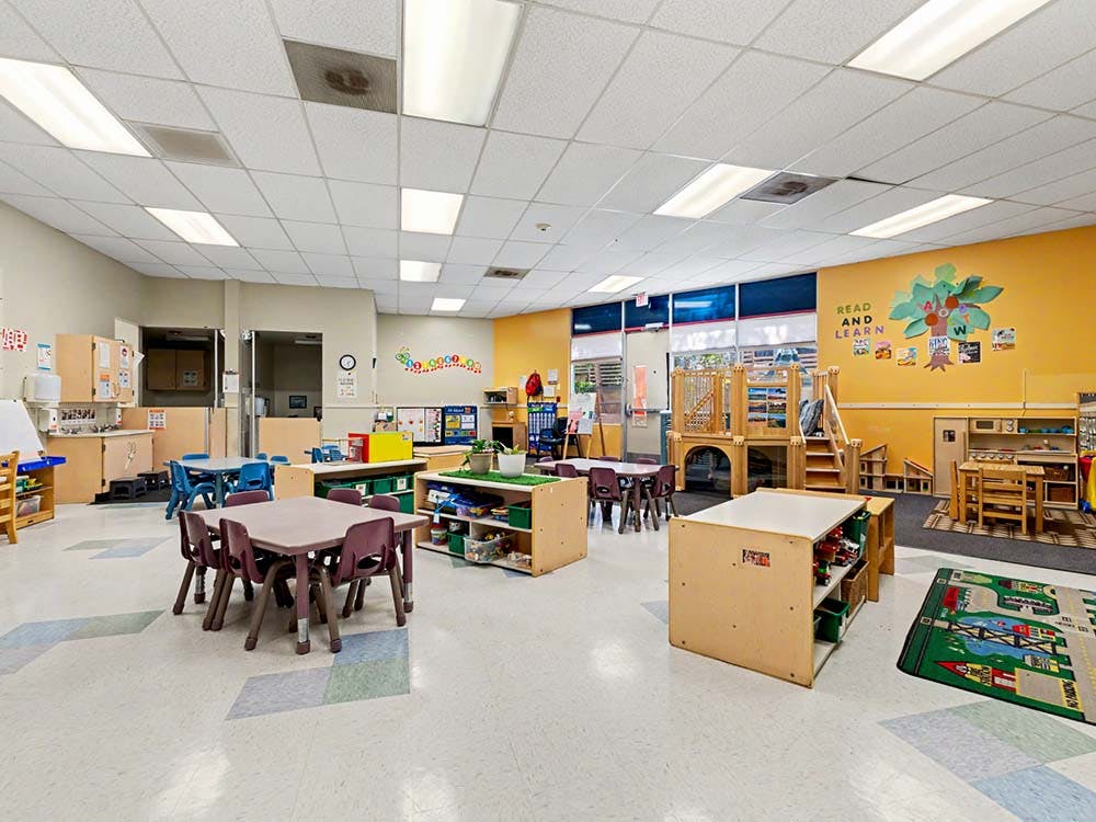 Empty classroom with small tables, chairs, and play equipment