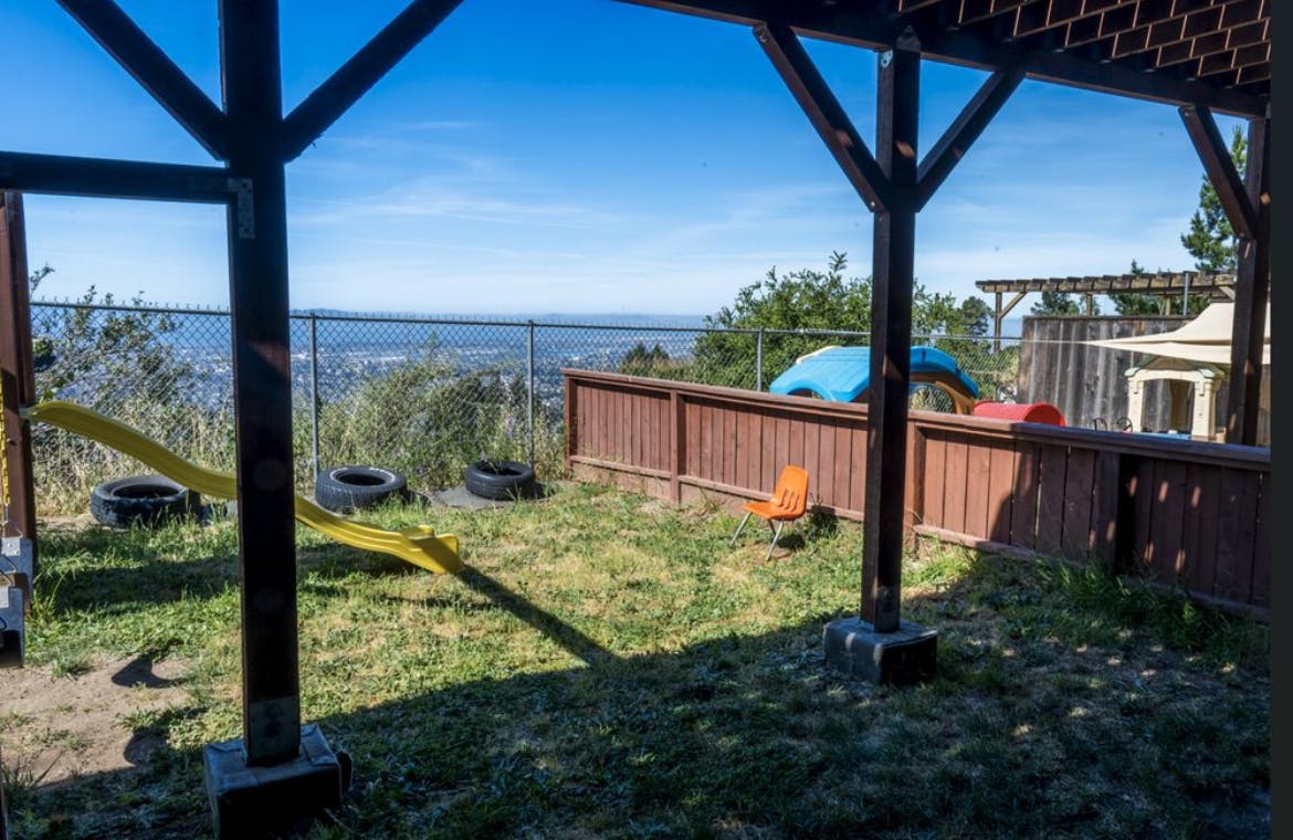 Playground equipment and a small chair in a fenced outdoor yard with a view