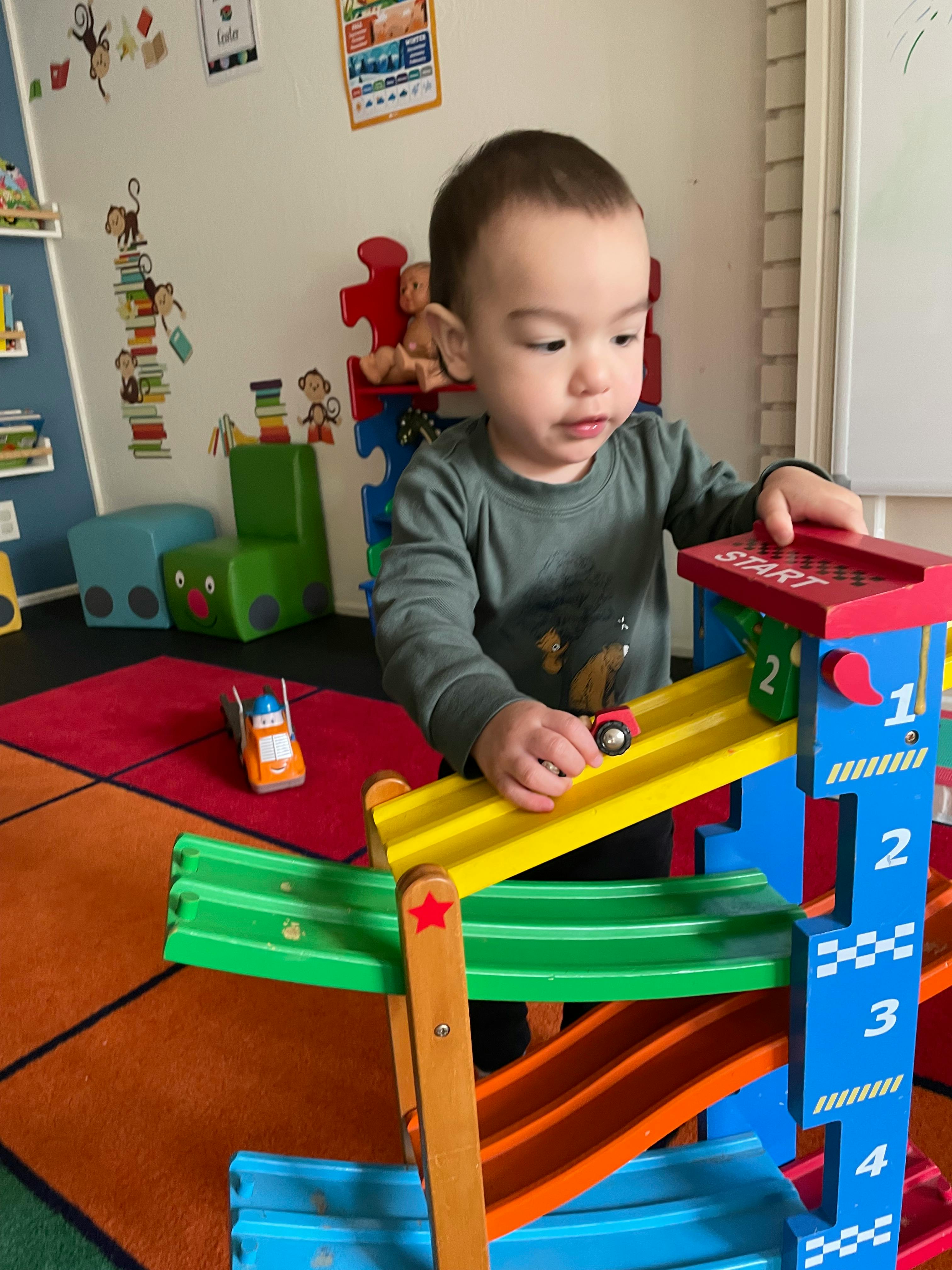 Child playing with a toy car on a ramp in a playroom