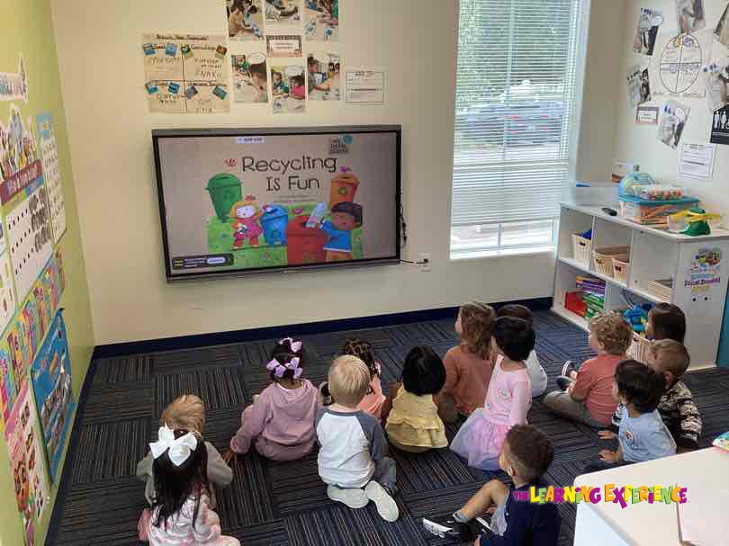 Group of young children sitting on a rug watching a screen in a classroom