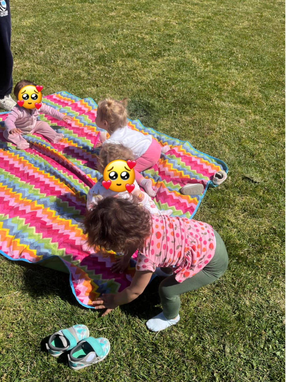 Multiple children playing on a colorful blanket on grass