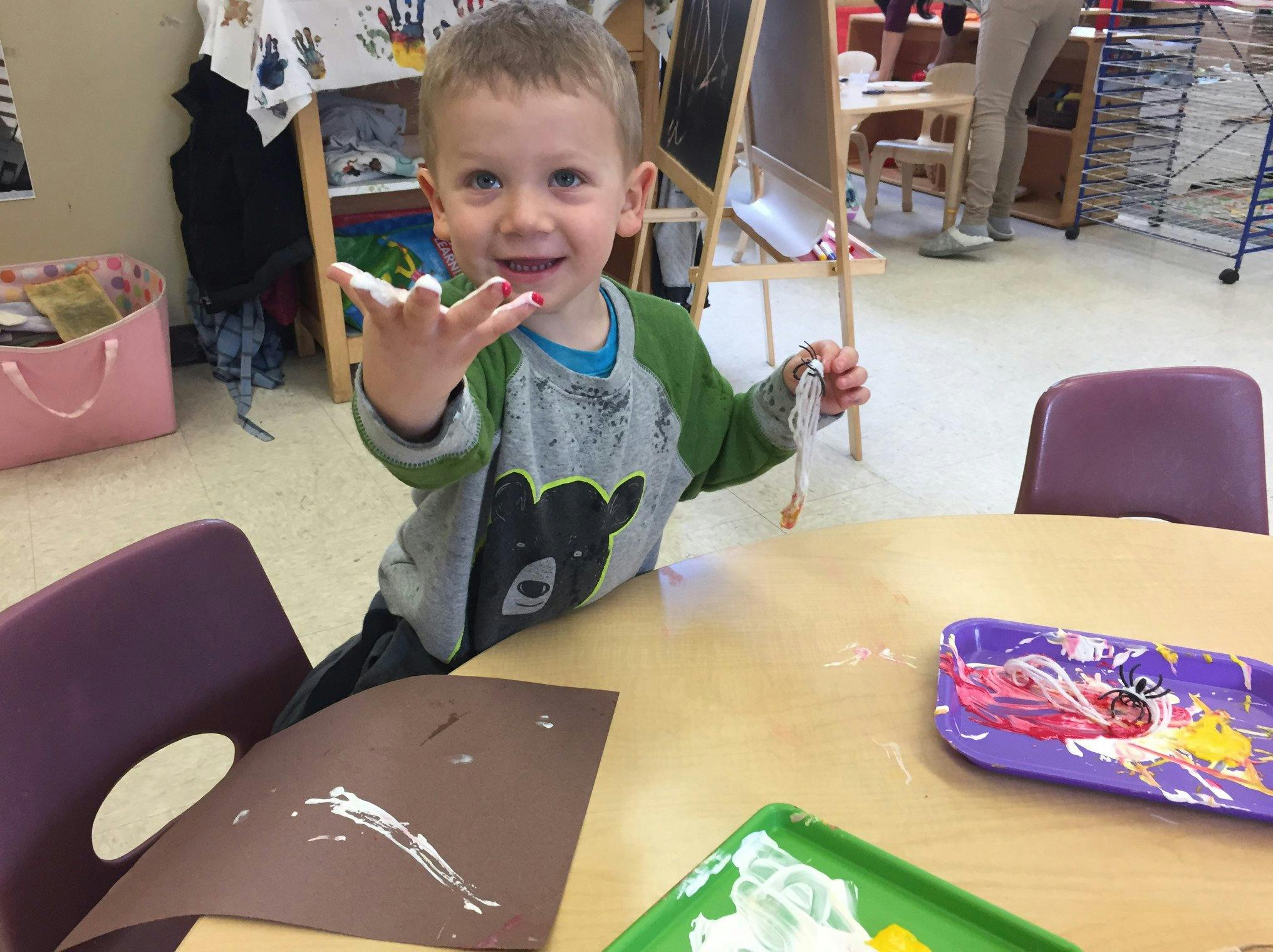Child at a table with paint on fingers and a painting tray