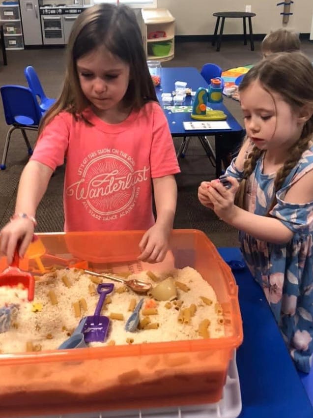 Two children playing with sand and toys in a sensory bin