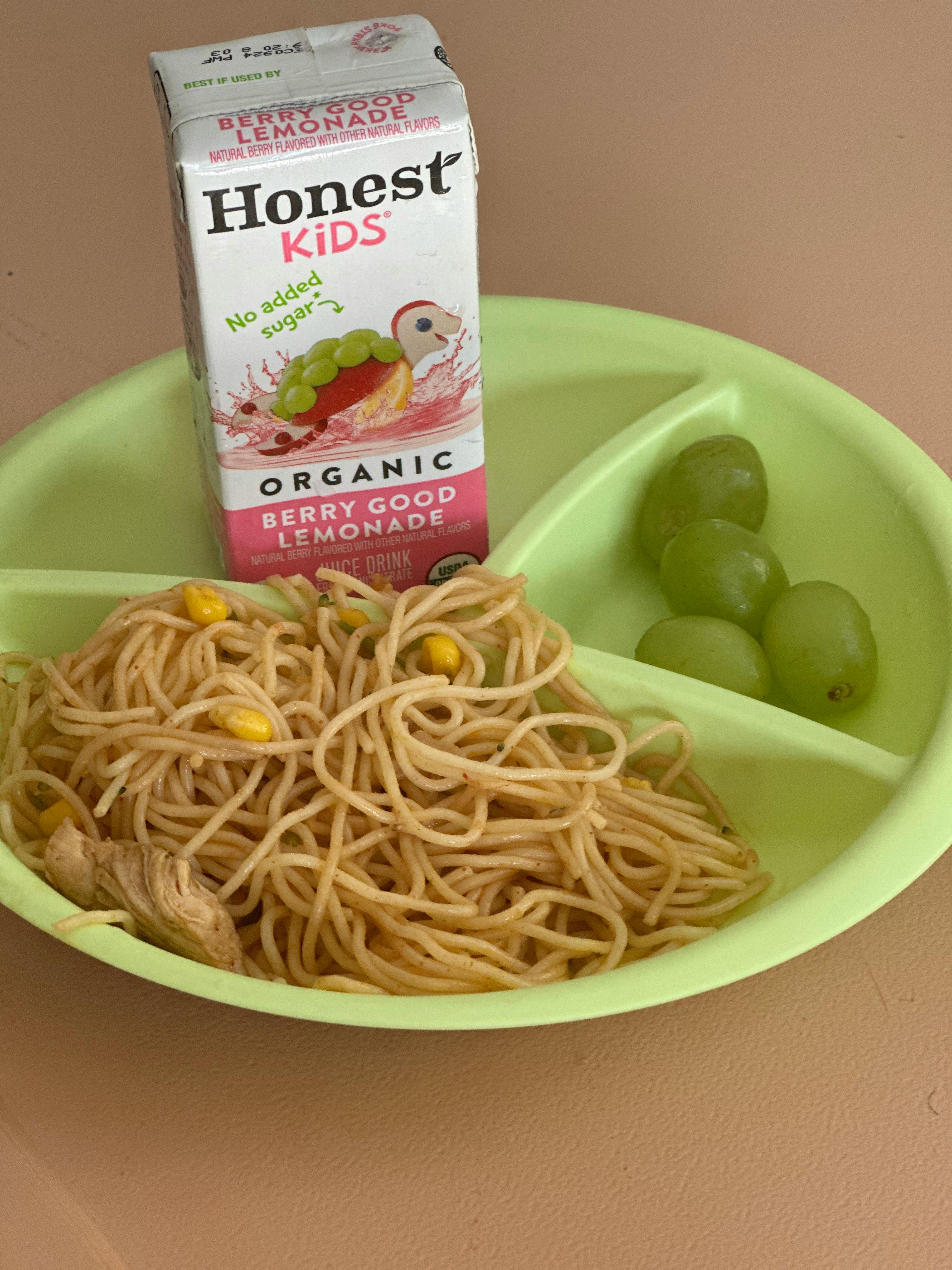 Spaghetti with corn, green grapes, and a juice box on a divided plate