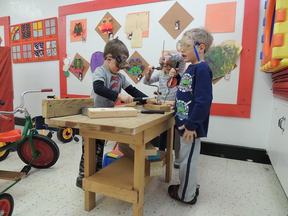 Children in safety glasses working at a small wooden workbench