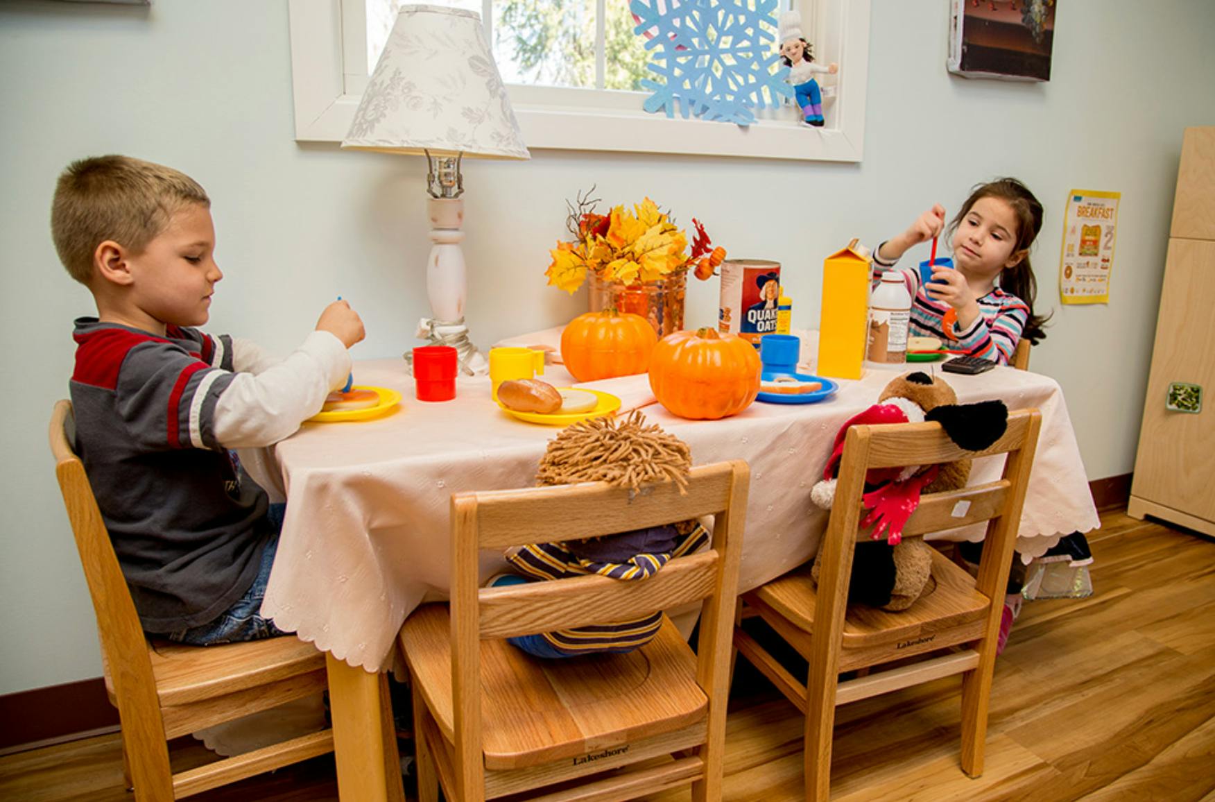 Two children sitting at a table with pumpkins and fall decorations