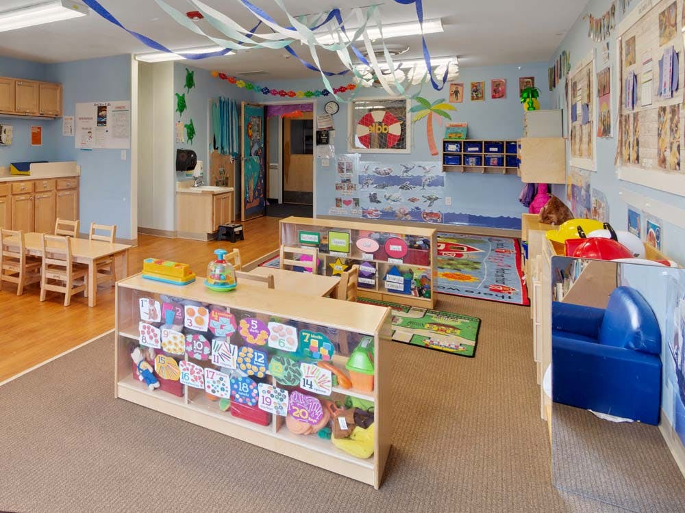 Classroom with child-sized tables and chairs, shelves with toys, and decorations