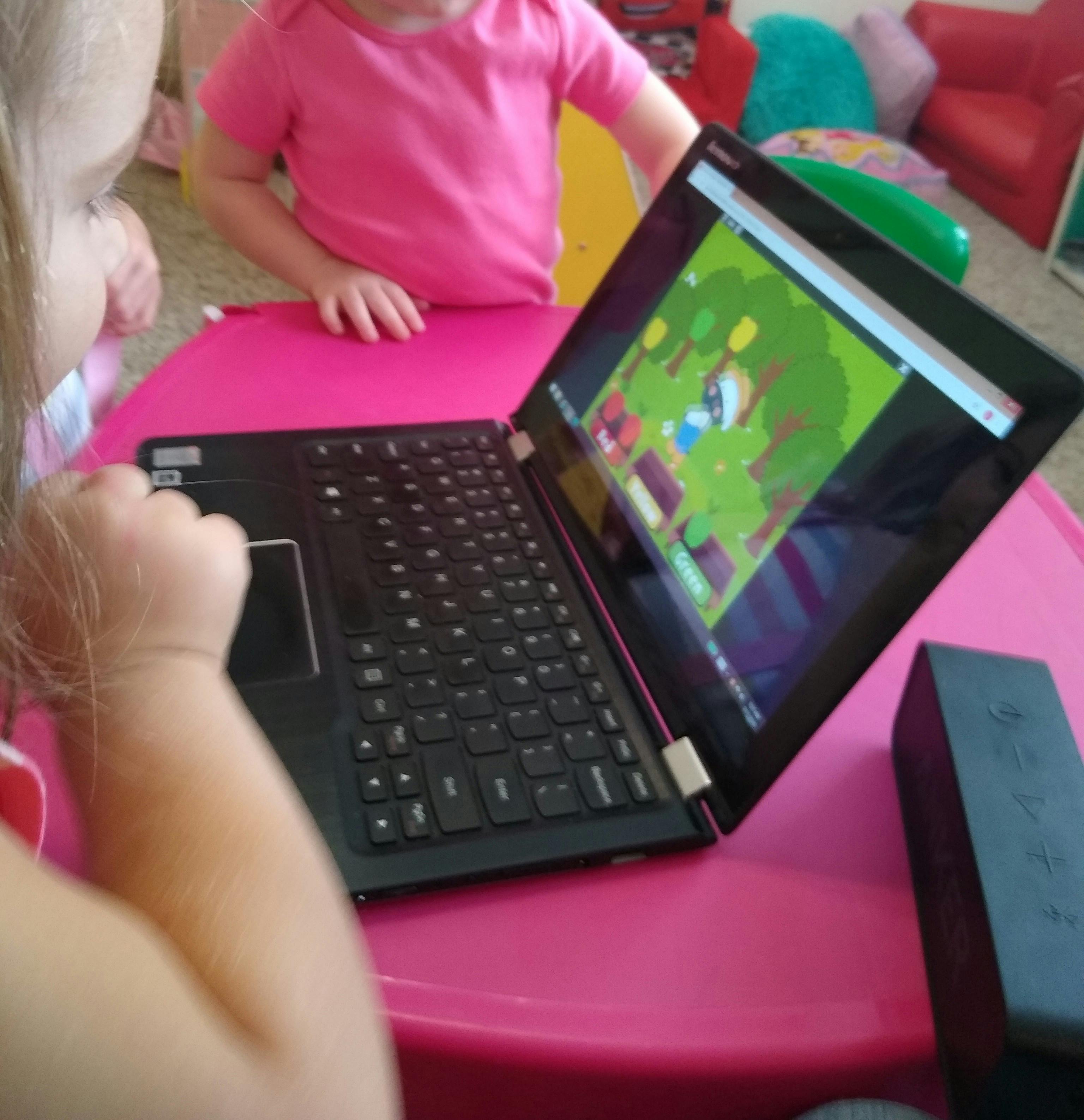 Child using a laptop with another child standing nearby