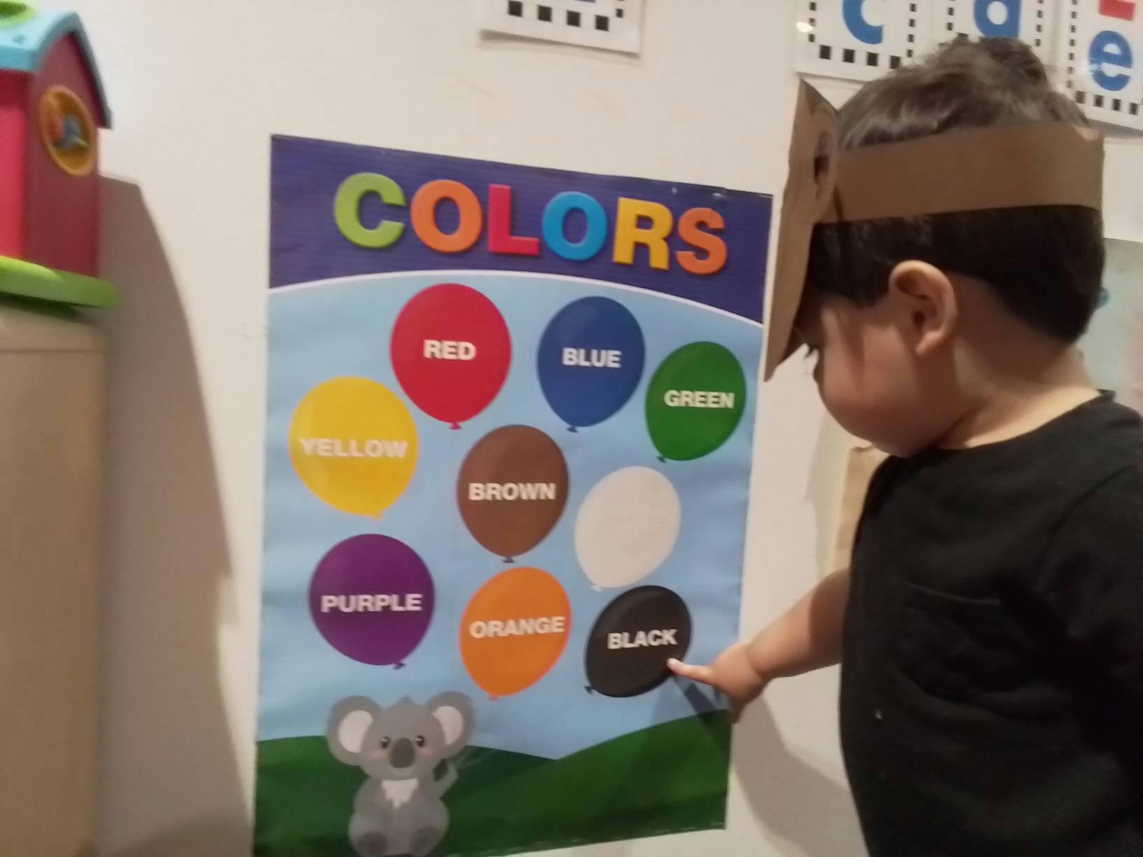 Child pointing at a colors chart with words chart