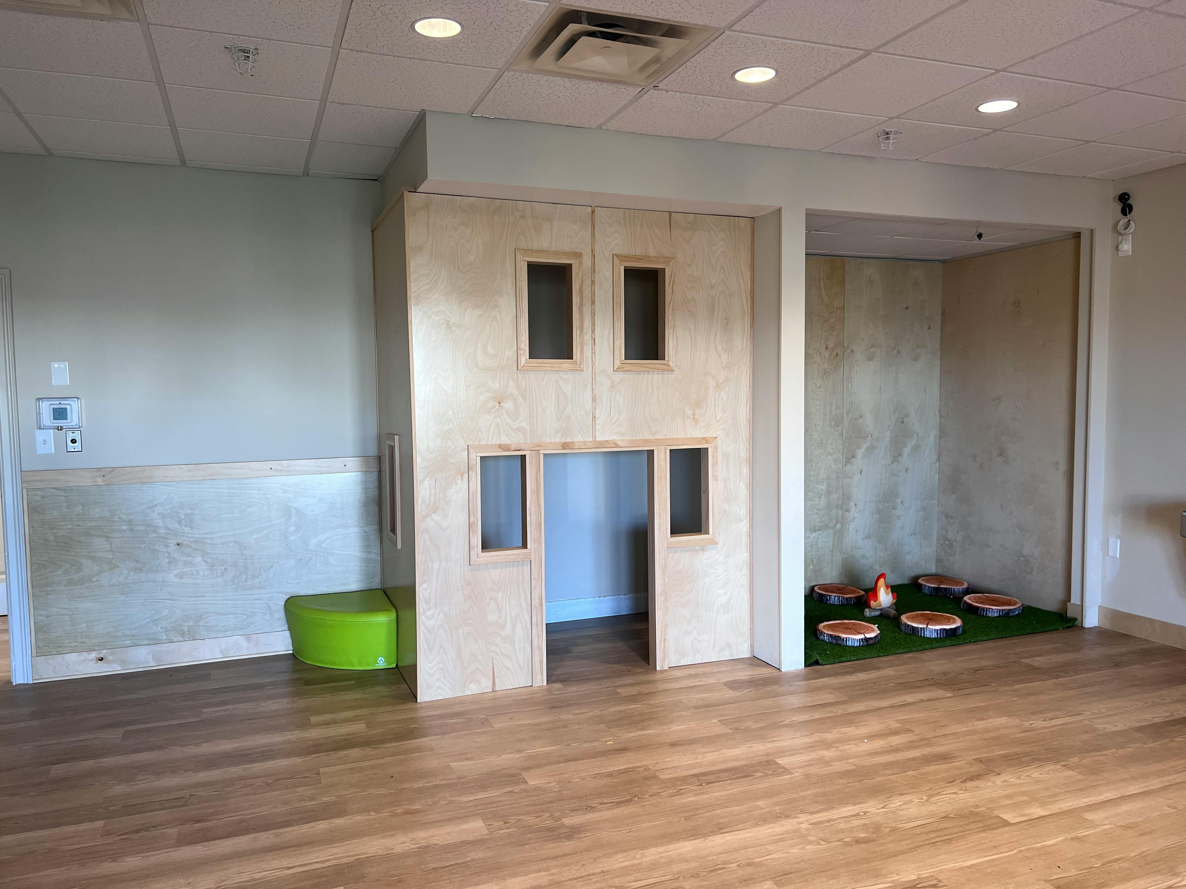 Indoor play area with a wooden playhouse and a green mat with bowls