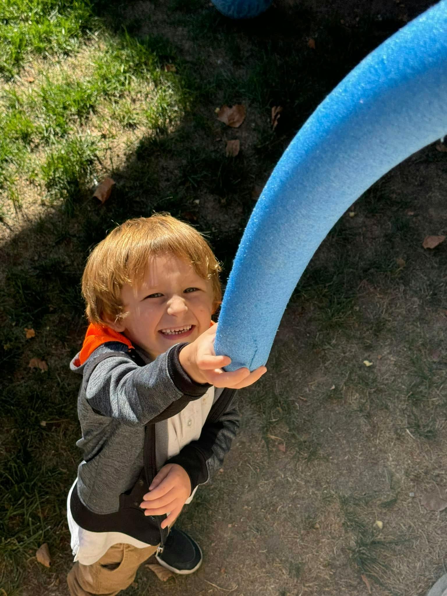 Child holding a foam pool noodle outdoors