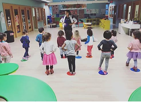 Adult and children standing on colorful spots in a classroom
